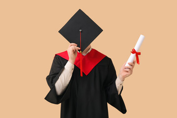 Male graduating student with mortar board and diploma on beige background