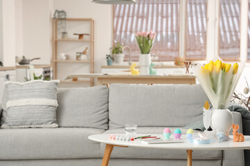 Vase with tulips, Easter rabbit, eggs and paints on table in living room
