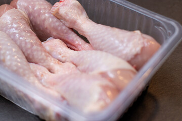 Close up of raw chicken drumstick in a plastic box on kitchen table 