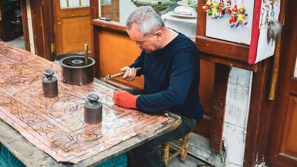 Copper craftsman shaping metal. Skilled artisan meticulously crafting intricate patterns on a copper sheet in a traditional workshop.