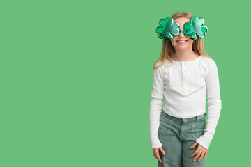 Cute little girl in decorative glasses in shape of clover on green background. St. Patrick's Day...