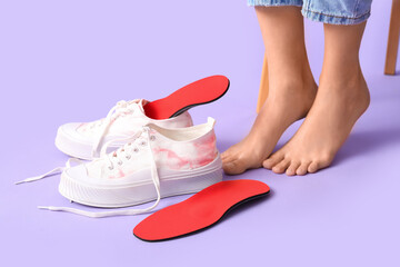 Naklejka premium Female legs near orthopedic insoles and sneakers on lilac background, closeup