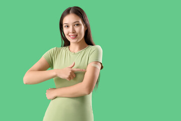Beautiful young woman pointing at applied medical patch on her arm against green background