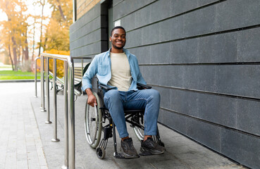Handicapped accessible city concept. Positive impaired Afro man in wheelchair leaving building on...
