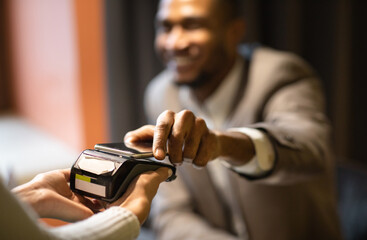 Contactless Payment System. Afro guy in suit holding smartphone close to electronic payment...