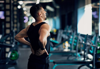 Obraz na płótnie Canvas Portrait Of Young Arab Bodybuilder Suffering Lower Back Pain At Gym, Upset Middle Eastern Male Athlete Rubbing Painful Sore Zone After Getting Sport Injury, Having Lumbar Spine Ache, Copy Space