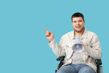 Young man in wheelchair with megaphone pointing at something on blue background