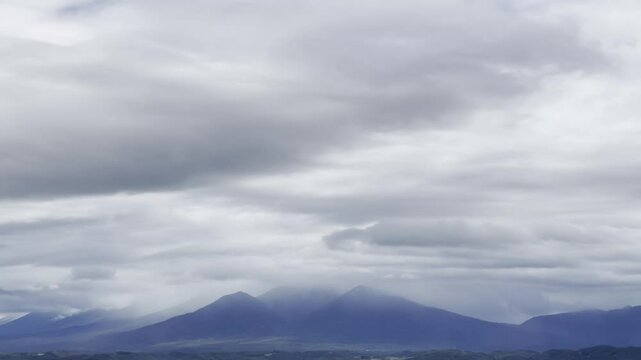 Soft, rolling clouds stretch across the sky, partially veiling the mountain peaks below. The overcast atmosphere creates a sense of mystery and tranquility