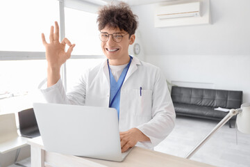 Male medical intern with laptop showing OK at reception in clinic