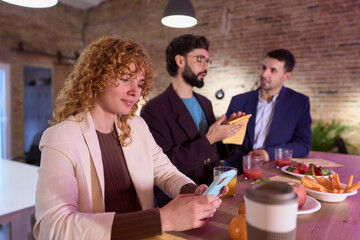 Businesswoman using smartphone during office break with colleagues chatting