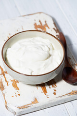 greek yogurt in a white bowl on a wooden board, vertical top view