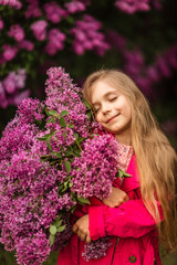 Fototapeta premium Cute little girl in pink coat holds big bouquet of lilacs in her hands and smiles in spring park near lilacs 