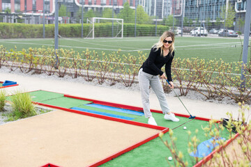 Woman playing mini golf and trying putting ball into hole. Summer leisure activity