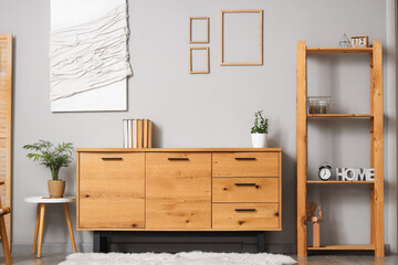 Wooden cabinet, shelving unit and houseplant near grey wall in room