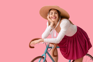 Beautiful young happy woman in wicket hat with bicycle on pink background