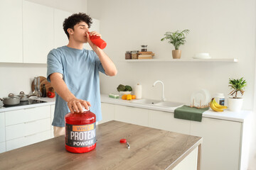 Sporty young man drinking protein shake in kitchen
