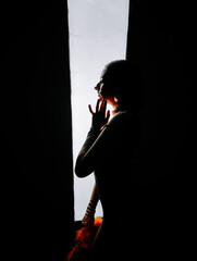 Naklejka premium Silhouette of a person in contemplation near a window surrounded by darkness