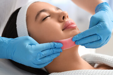 Naklejka premium Beautician removing woman's hair on face with wax strip in salon, closeup