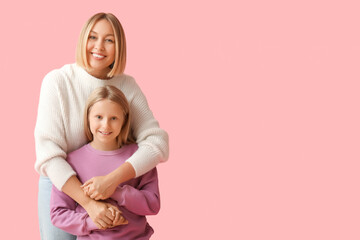 Beautiful woman hugging her cute daughter in stylish sweaters on pink background