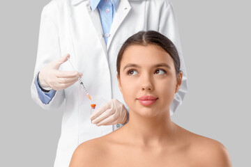 Naklejka premium Cosmetologist holding ampule with syringe and beautiful young woman on grey background. Plastic surgery concept