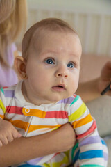 Fototapeta premium A young mother looks at her phone while her baby crawls on the bed next to her