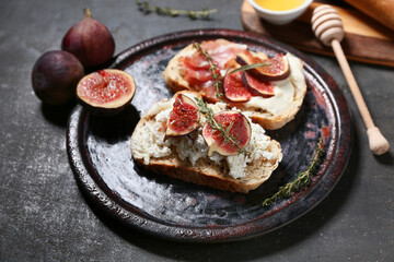 Plate of delicious fig bruschetta with ricotta cheese on black background, closeup