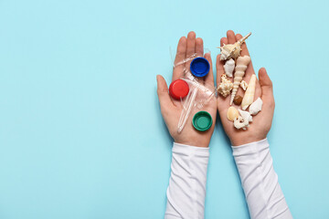 Female hands with seashells and plastic on blue background. Microplastic Awareness Month