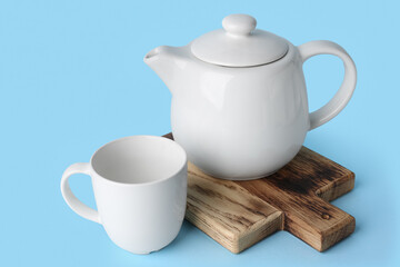 White ceramic empty mug and tea pot on board on blue background