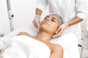 Cosmetologist applying cream on female face in cosmetology salon.
