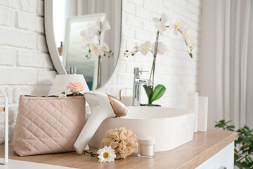 Modern photoepilator with cosmetic bag, bath sponge and flowers on table near sink in bathroom