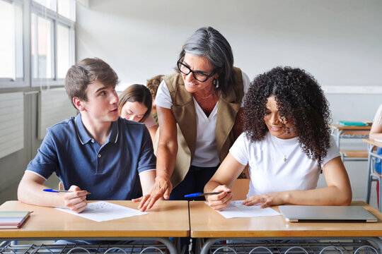 Mature teacher helping teenager students during exam in High School classroom
