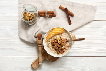 Composition with bowl of tasty oatmeal, pieces of apple and nuts on white wooden background