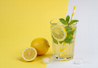 Fototapeta premium Chilled lemonade in a glass with fresh mint and citrus on a yellow and white backdrop