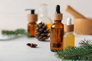 Bottles with coniferous cone essential oil on white wooden background