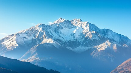 Naklejka premium The sunrise illuminates a snow-covered mountain peak against a clear blue sky