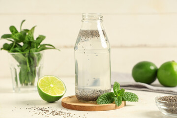 Bottle of water with chia seeds, limes and mint on white table against wooden background