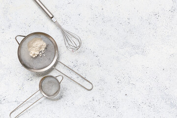 Metal sieves with flour and whisk on light background