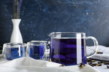 Teapot and cups of butterfly pea flower tea on blue background