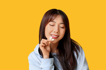 Fototapeta premium Pretty young Asian woman with chewing gums on yellow background