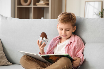 Little boy with chocolate egg reading book in living room