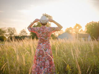 Young woman walking through picturesque European field in late summer. Golden sunlight, lush...