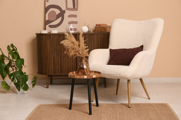 Interior of living room with armchair, coffee table and home decor on commode near brown wall