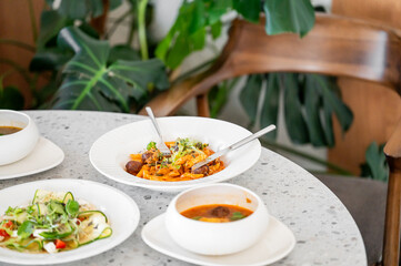 A beautifully arranged table featuring a variety of dishes, including a colorful salad, a spicy soup, and a vibrant main course, surrounded by lush greenery