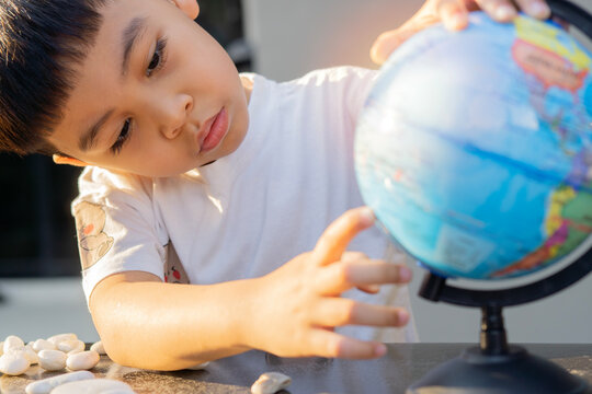 Close-up portrait of little Asian boy pointing a spot on the globe at outdoor in the evening