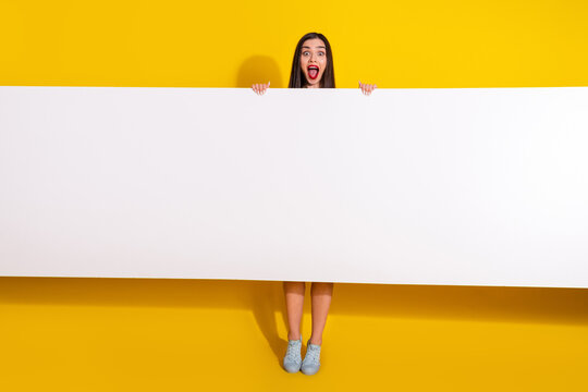 Excited young woman holding blank white banner with yellow background, promoting concepts or messages with bright and cheerful appearance.
