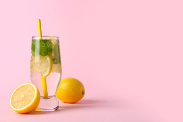Glass of water with lemons, mint leaves and straw on pink background