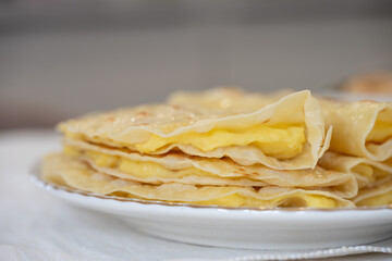 Thin pancakes with custard filling forming a stack on a white plate, representing a traditional breakfast or dessert