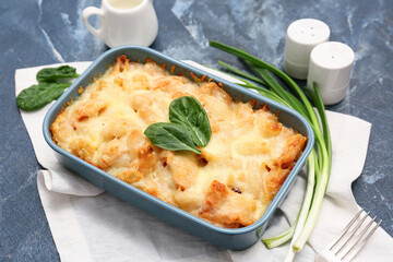 Baking dish with tasty pasta, spinach leaves and green onion on blue grunge background