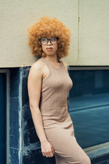 Fashion model posing confidently near a wall, showcasing a stylish beige dress paired with...
