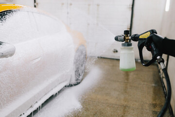 Worker sprays soap solution with pressure from water jet for detailing car wash. Application of...
